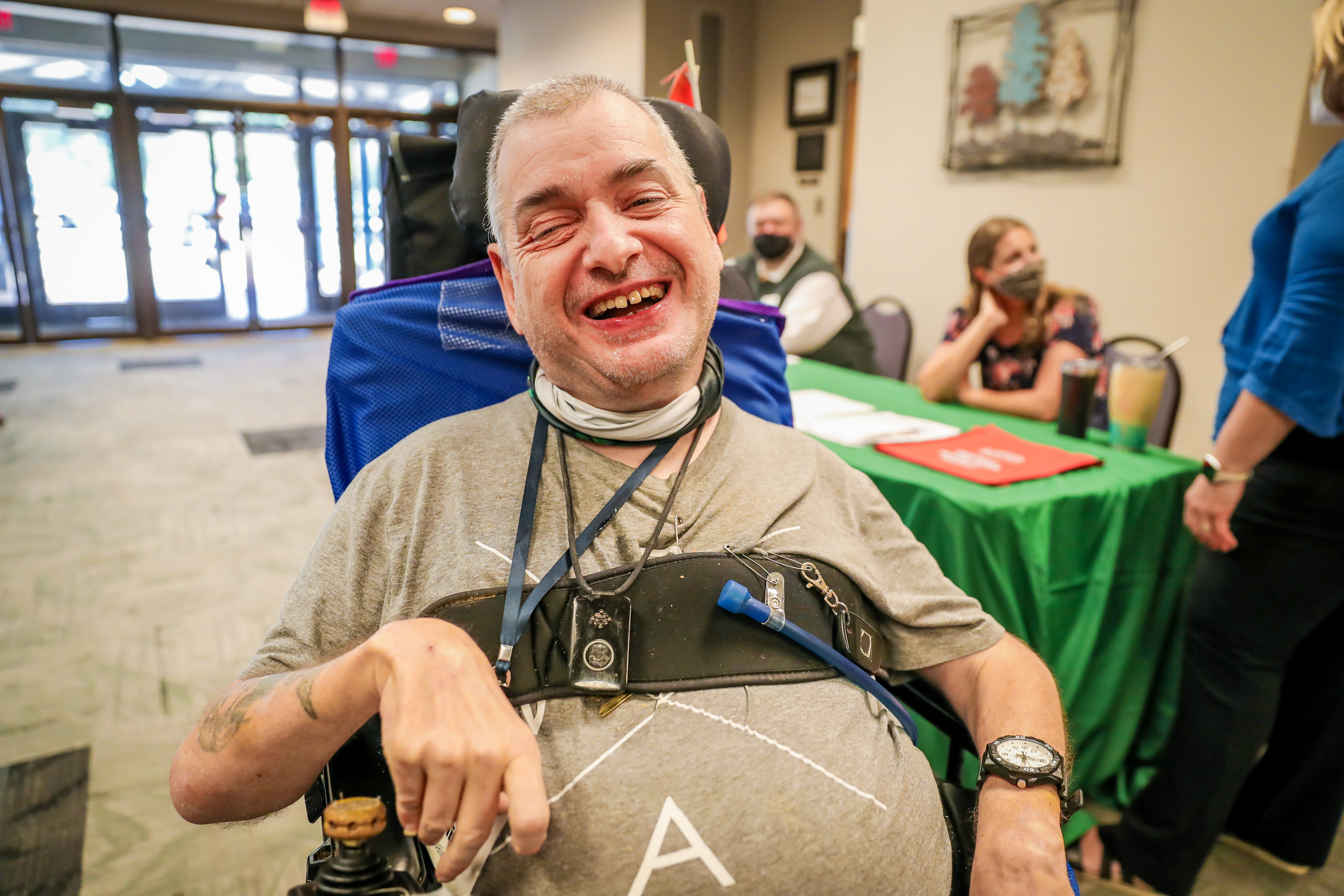 A male participant at the Caucus smiles big for the camera. He is using a wheelchair for mobility.
